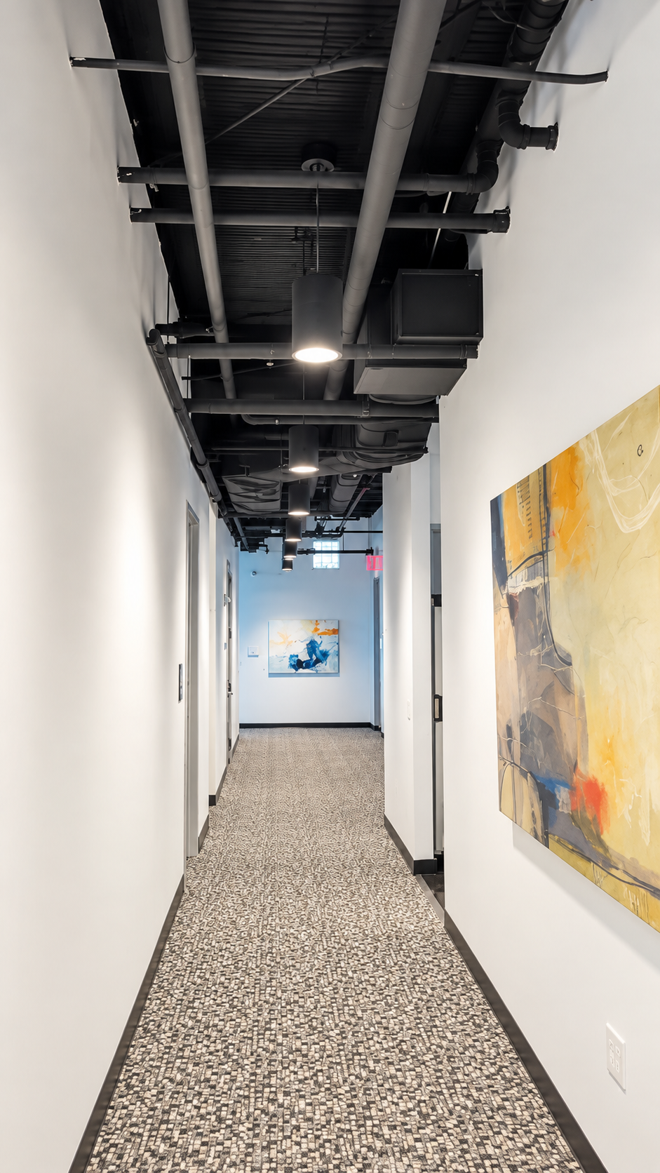 Long commercial corridor with exposed ceilings and contemporary artwork